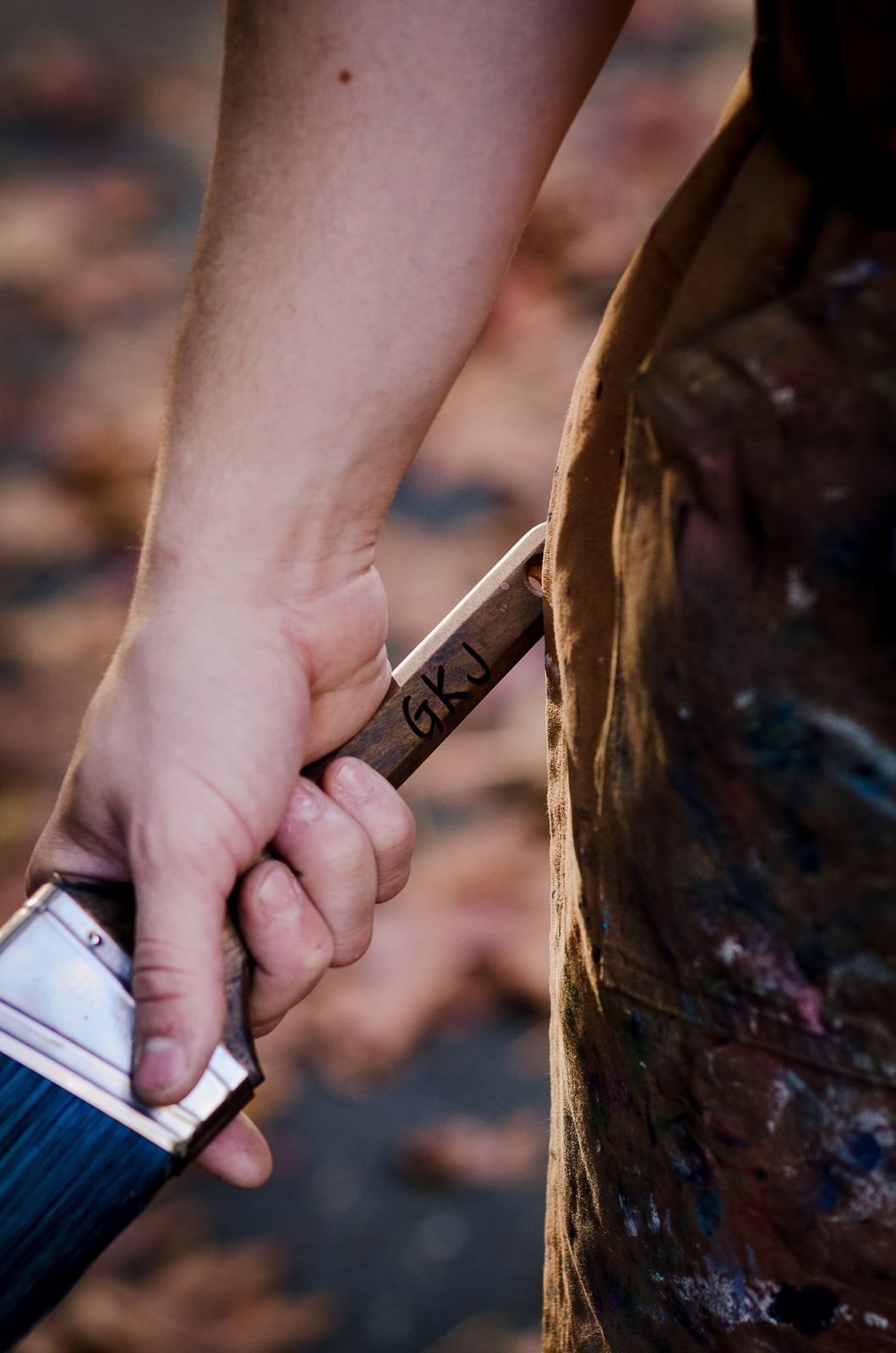 The artist's hand gripping a wide house-painting brush, a paint-stained work apron behind.